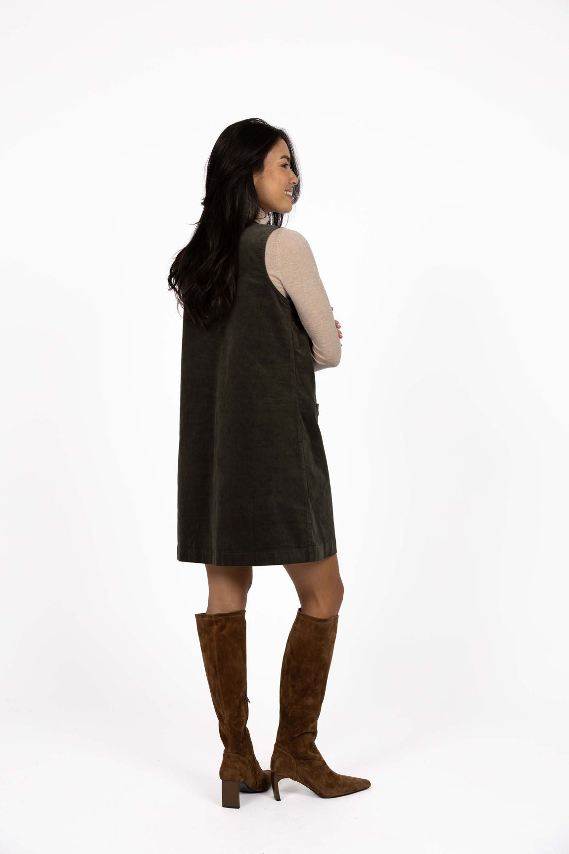 Model in studio wearing Nova Cord Dress in Khaki over the Alana Skivvy in Birch with brown boots, full-length back view 