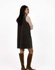 Model in studio wearing Nova Cord Dress in Khaki over the Alana Skivvy in Birch with brown boots, full-length back view 