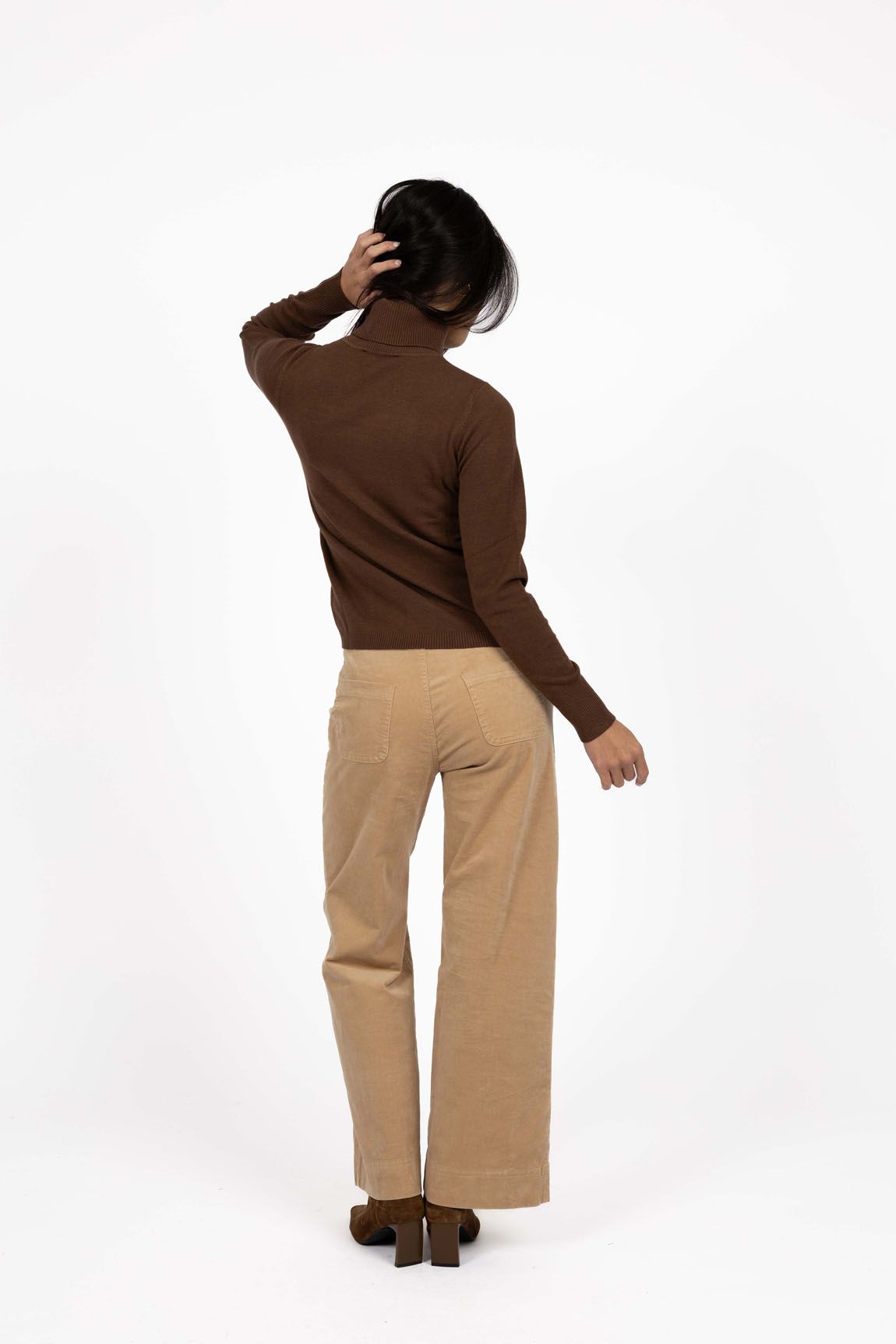 Model in studio wearing Alana Skivvy in Chocolate with Va Va Velour Pant in Camel and brown boots, full-length back view  