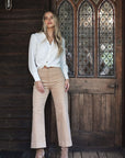 Model in lifestyle setting wearing Pixie Shirt in White with Fleetwood Cord Pant in Wheat, full-length front view against wooden door  