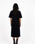 Model in studio wearing Amici Cord Dress in Indigo with brown boots, full-length back view  