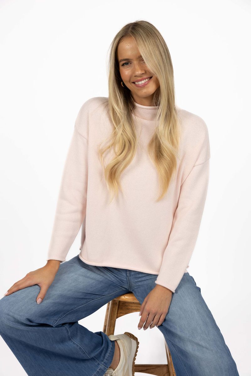 Model in studio wearing Divine Jumper in Pink with Ryder Jean, close-up front view sitting on wooden stool 