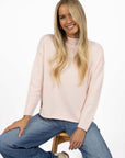 Model in studio wearing Divine Jumper in Pink with Ryder Jean, close-up front view sitting on wooden stool 