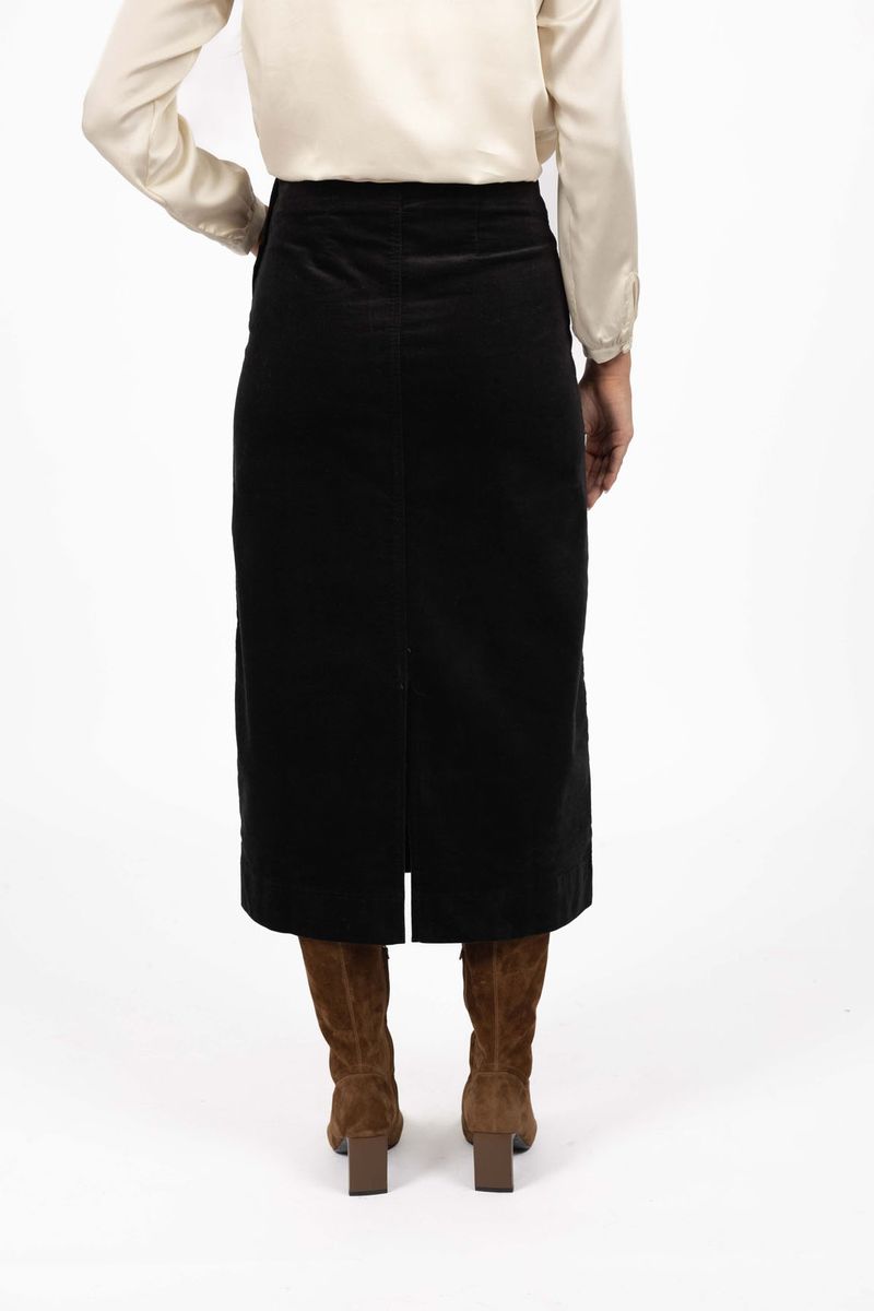 Model in studio wearing Va Va Velour Skirt in Black with brown boots, close-up back view showing midi length and vent  
