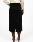 Model in studio wearing Va Va Velour Skirt in Black with brown boots, close-up back view showing midi length and vent  