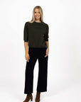 Model in studio wearing Grace Top in Moss with black Va Va Velour Pant and brown boots, full-length front view 