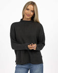 Model in studio wearing Divine Jumper in Charcoal with Ryder Jean, close-up front view showing rolled cuffs, hem and collar 
