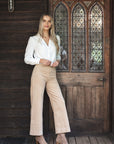 Model in lifestyle setting wearing Fleetwood Cord Pant in Wheat with Pixie Shirt in White, full-length front view against wooden door  