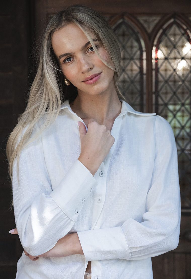 Model in lifestyle setting wearing Pixie Shirt in White, close-up front view showing button closure cuffs 