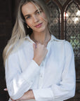 Model in lifestyle setting wearing Pixie Shirt in White, close-up front view showing button closure cuffs 