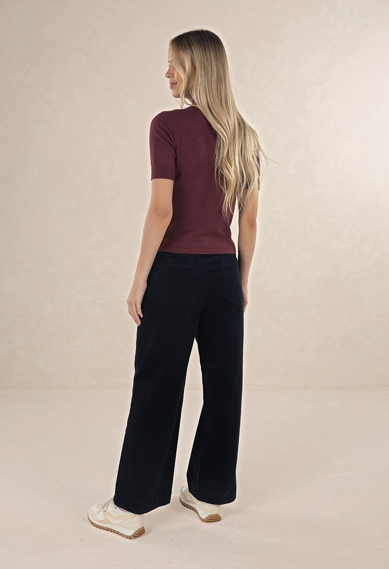Model in studio wearing Suki Cord Pant in Indigo and Vera Top in Claret with cream sneakers, full-length back view 