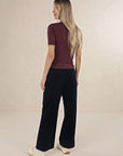 Model in studio wearing Suki Cord Pant in Indigo and Vera Top in Claret with cream sneakers, full-length back view 