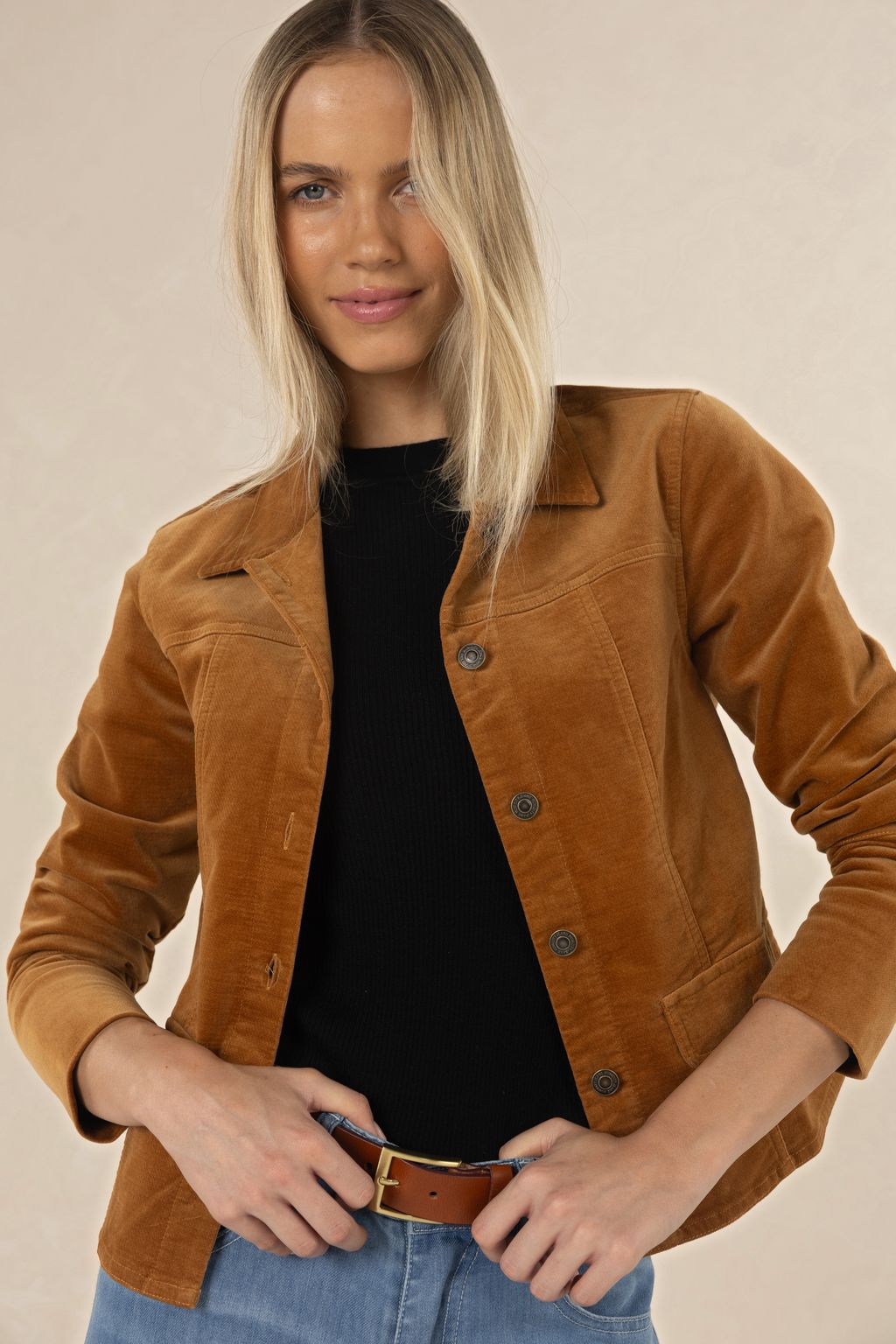 Model in studio wearing Gabi Jacket in Camel over black tee and Ryder Jean with tan Classic Belt, close-up front view holding belt  
