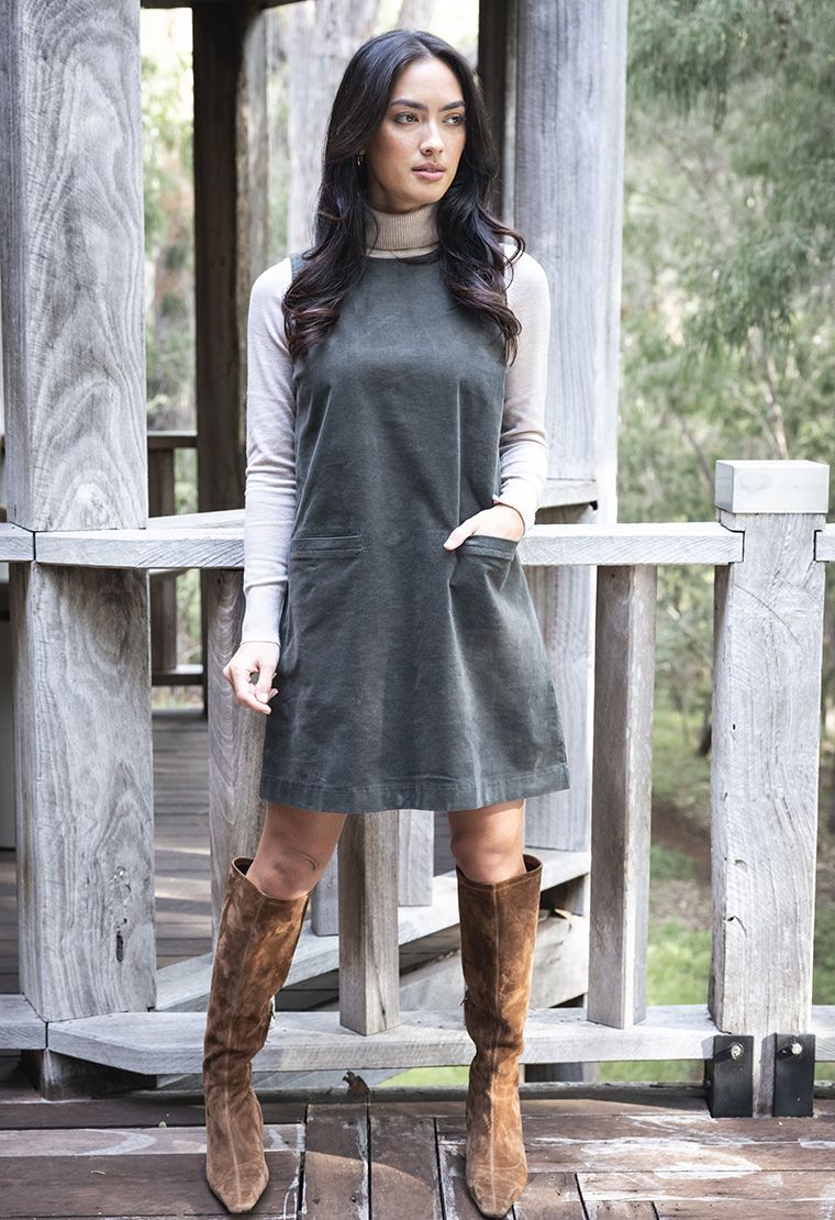Model in lifestyle setting wearing Nova Cord Dress in Khaki over the Alana Skivvy in Birch with brown boots, full-length front view  