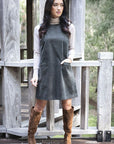Model in lifestyle setting wearing Nova Cord Dress in Khaki over the Alana Skivvy in Birch with brown boots, full-length front view  
