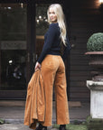 Model in lifestyle setting wearing Stitched Luxe Pant in Camel with Tempo Top in Black holding matching Va Va Velour Coat, full-length back view  