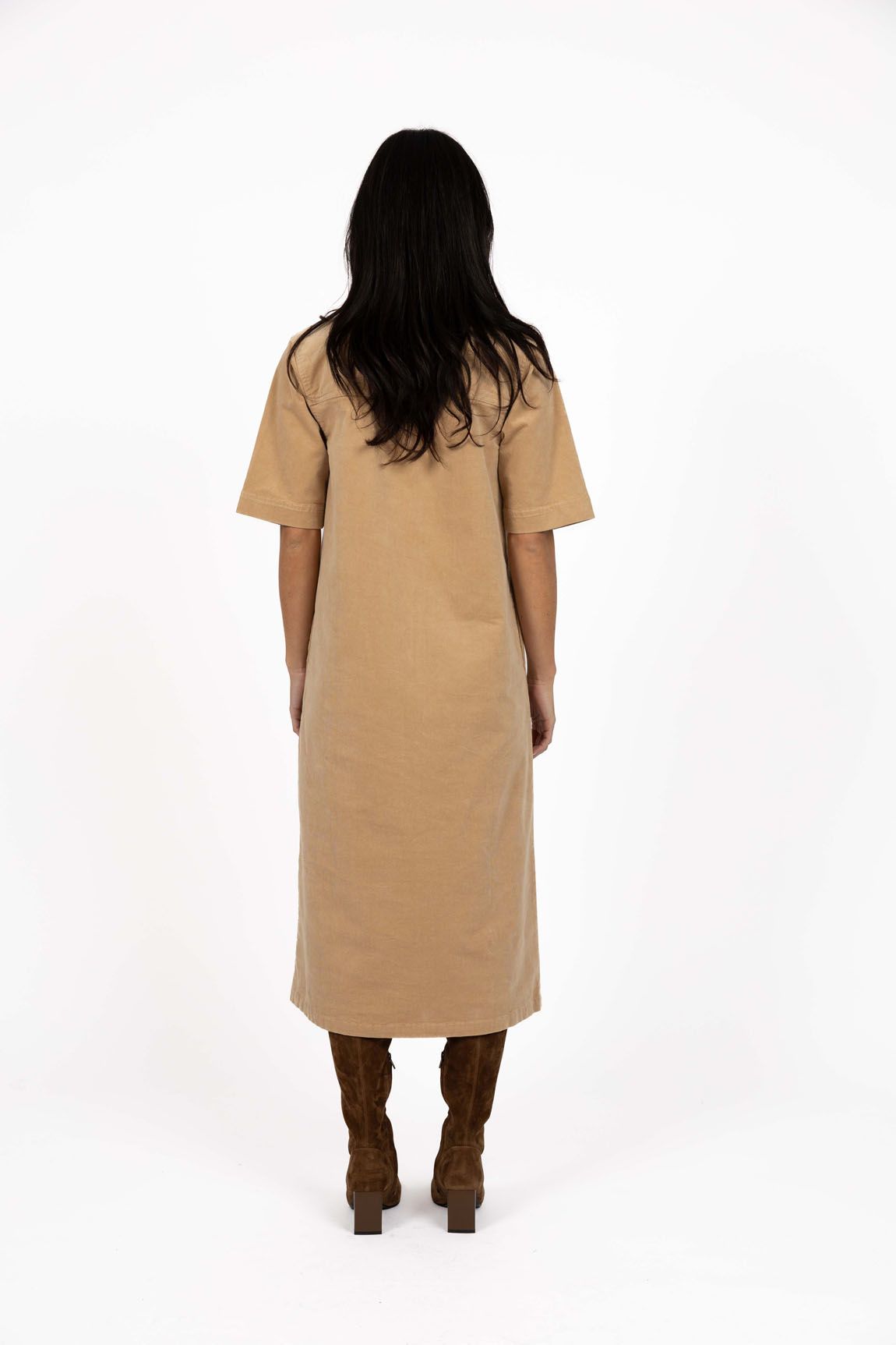 Model in studio wearing Amici Cord Dress in Wheat with brown boots, full-length back view 