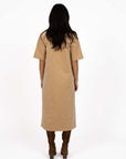 Model in studio wearing Amici Cord Dress in Wheat with brown boots, full-length back view 