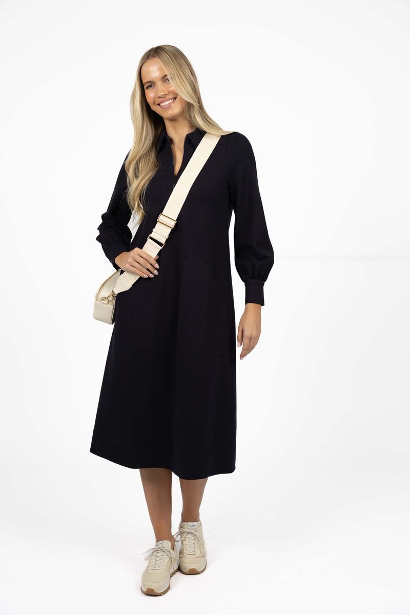 Model in studio wearing Dune Midi Dress in Navy with white bag and sneakers, full-length front view  