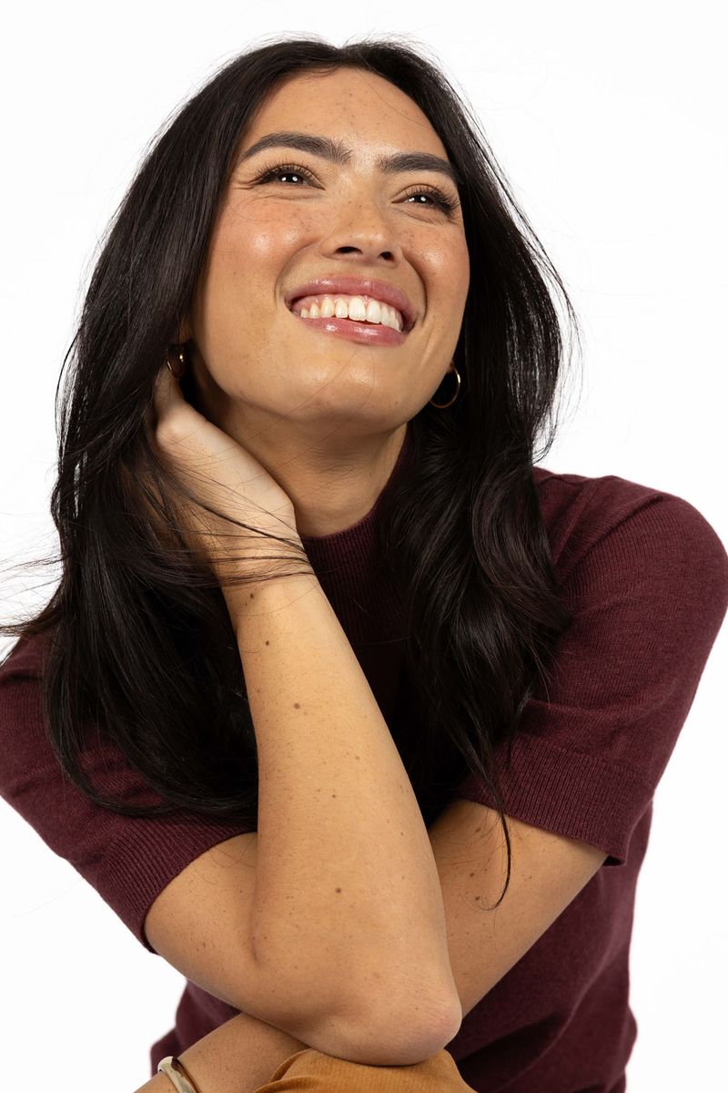 Model in studio wearing Vera Top in Claret, close-up front view with crossed arms and a big smile 