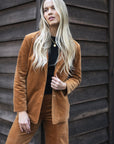 Model in lifestyle setting wearing Va Va Velour Coat in Camel over black top with matching Stitched Luxe Pant, close-up front view  