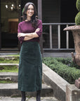 Model in lifestyle setting wearing Grace Top in Merlot with Va Va Velour Skirt in Pine, full-length front view on mossy stairs  
