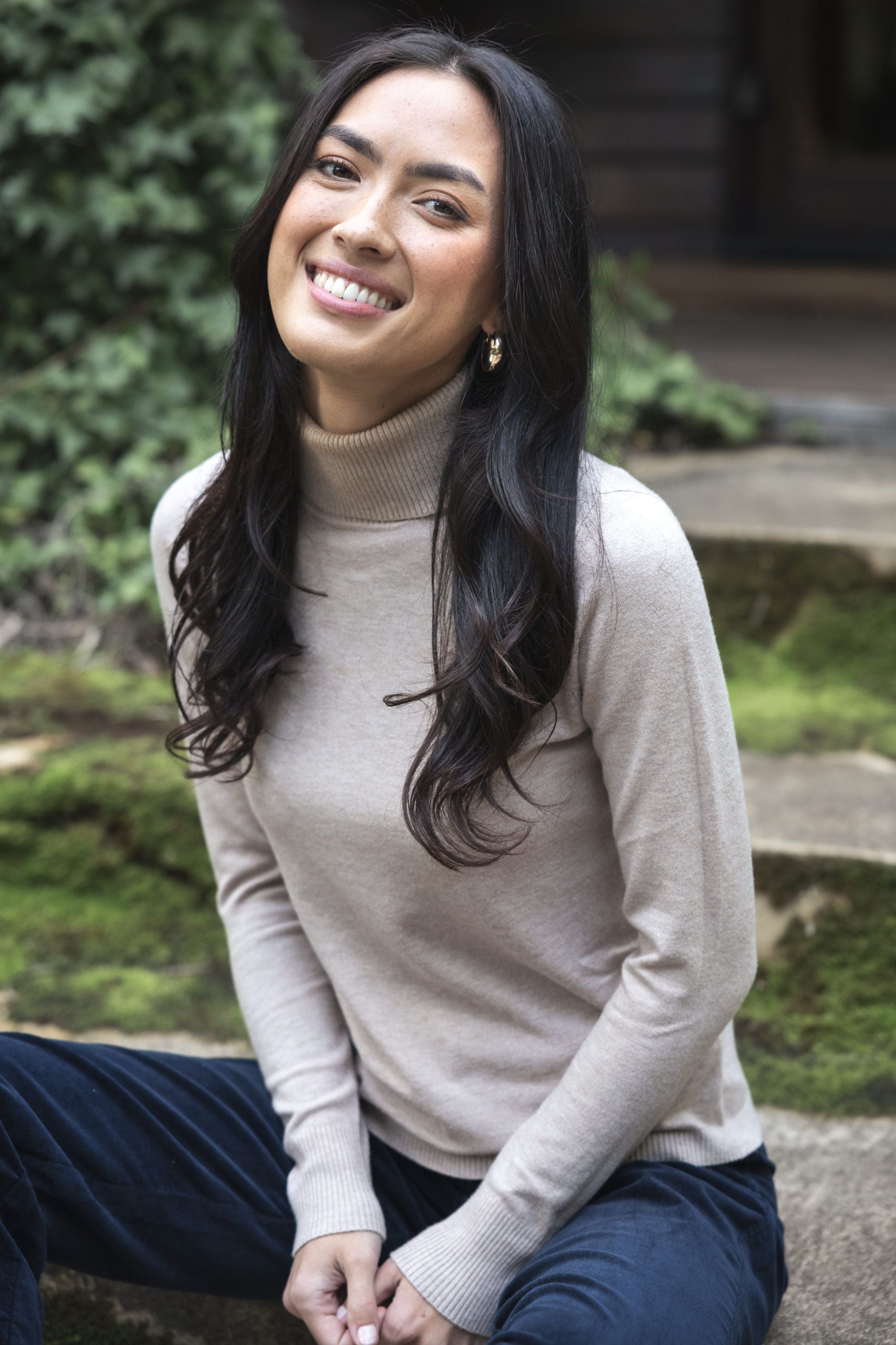 Model in lifestyle setting wearing Alana Skivvy in Birch with Va Va Velour Pant in Navy, close-up front view sitting on stone steps 