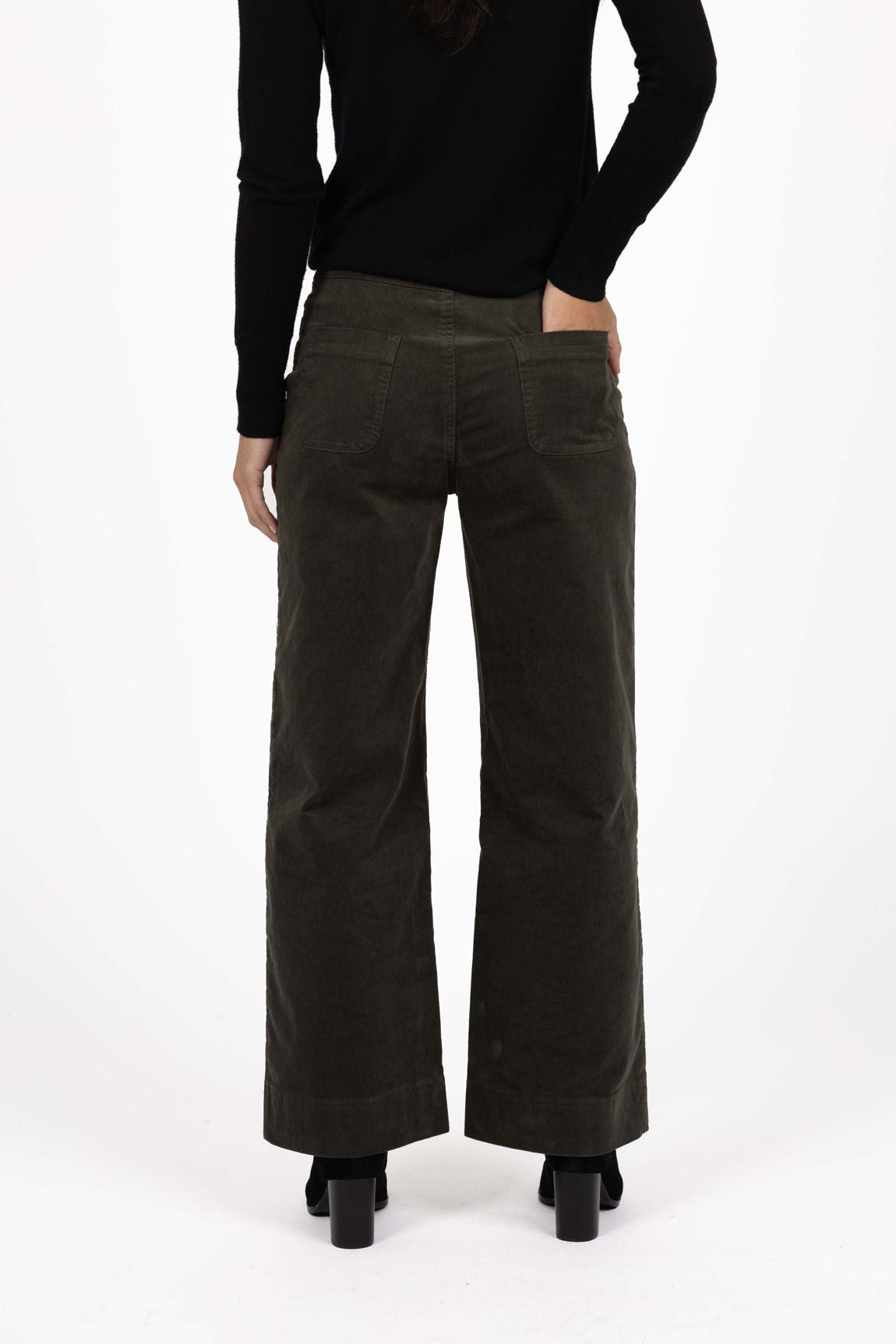 Model in studio wearing Fleetwood Cord Pant in Khaki with black Alana Skivvy and black boots, close-up back view with one hand in pocket 