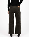 Model in studio wearing Fleetwood Cord Pant in Khaki with black Alana Skivvy and black boots, close-up back view with one hand in pocket 