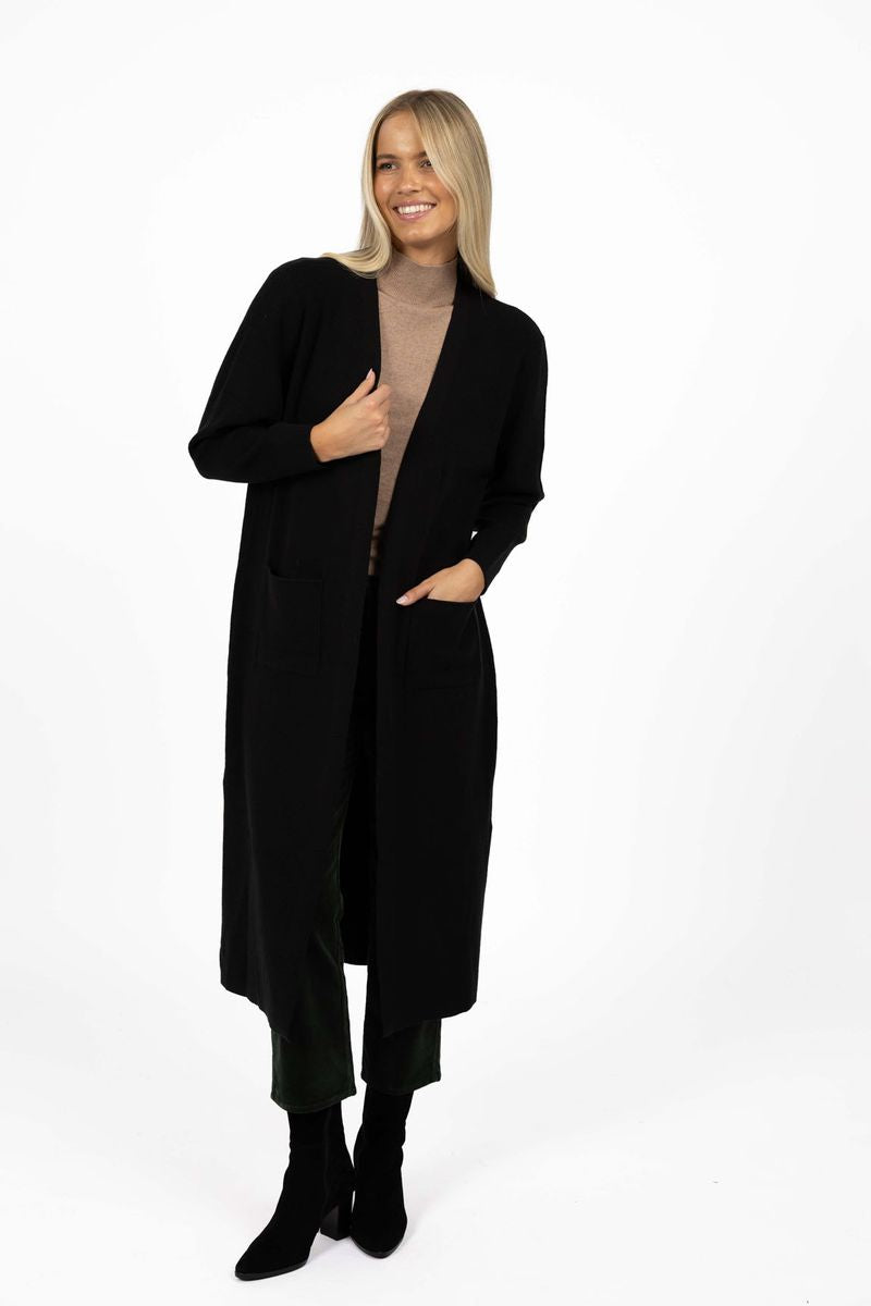 Model in studio wearing Clover Cardi in Black over Vera Top in Hazelnut and Va Va Velour Pant in Pine with black boots, full-length front view  