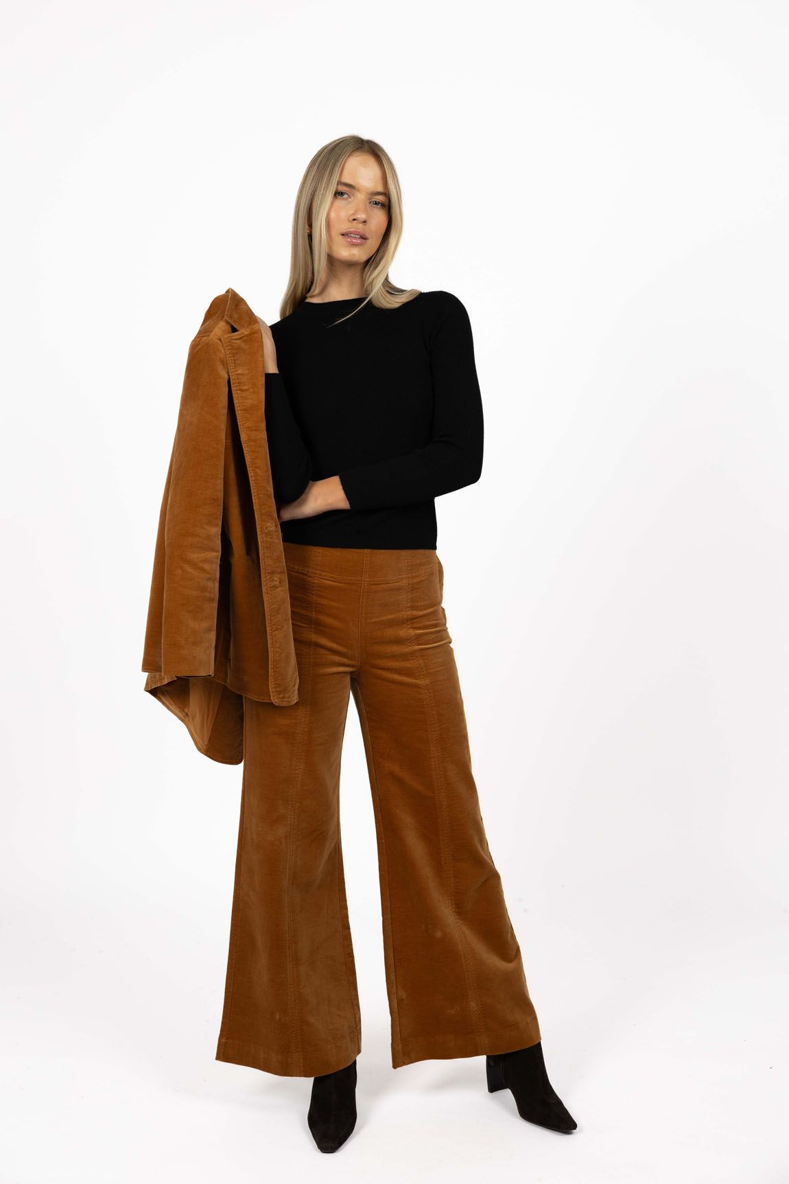 Model in studio wearing Stitched Luxe Pant in Camel with Tempo Top in Black holding matching Va Va Velour Coat, full-length front view  