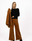 Model in studio wearing Stitched Luxe Pant in Camel with Tempo Top in Black holding matching Va Va Velour Coat, full-length front view  