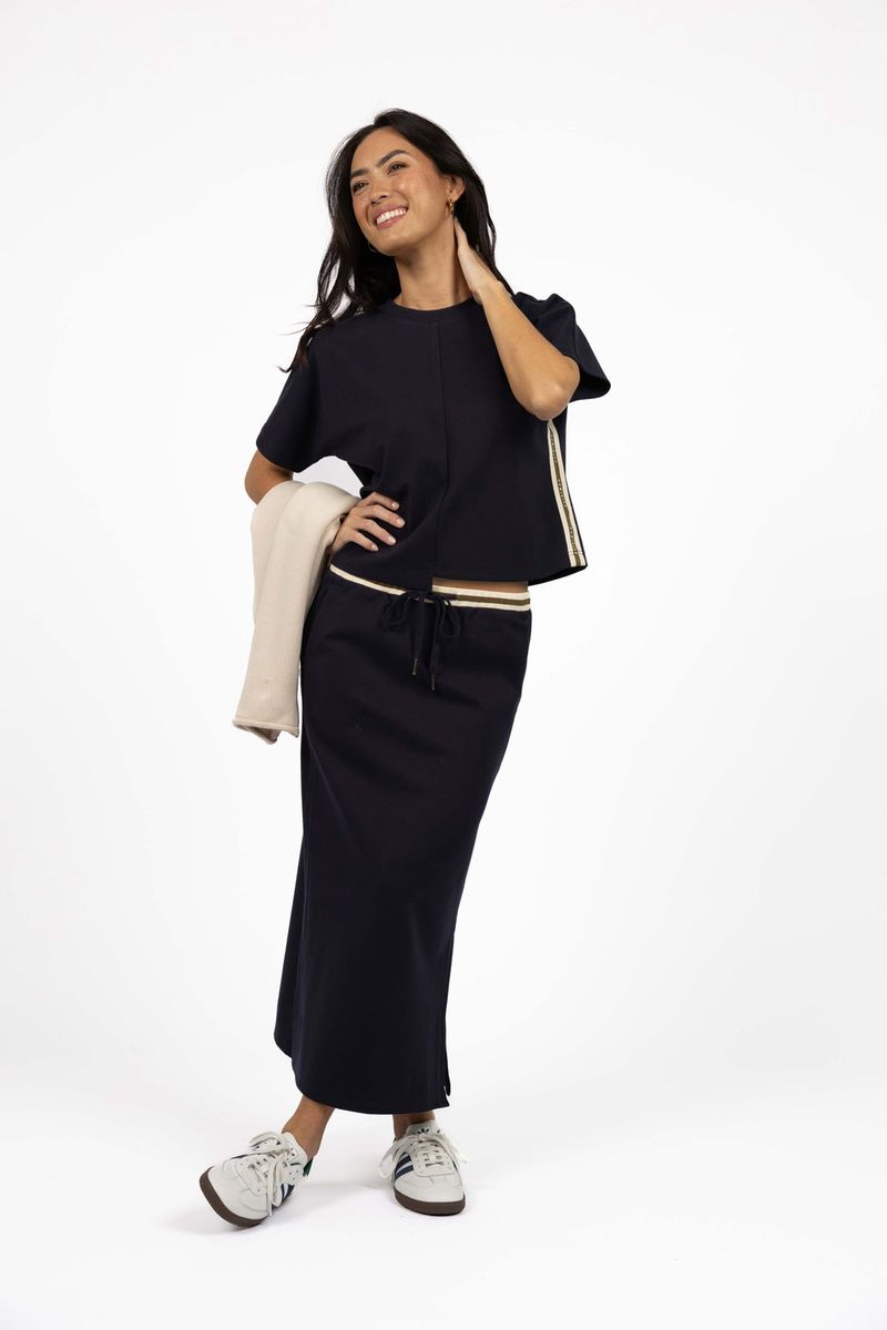 Model in studio wearing Roca Skirt in Navy with matching Mosh Top and white sneakers, full-length front view 
