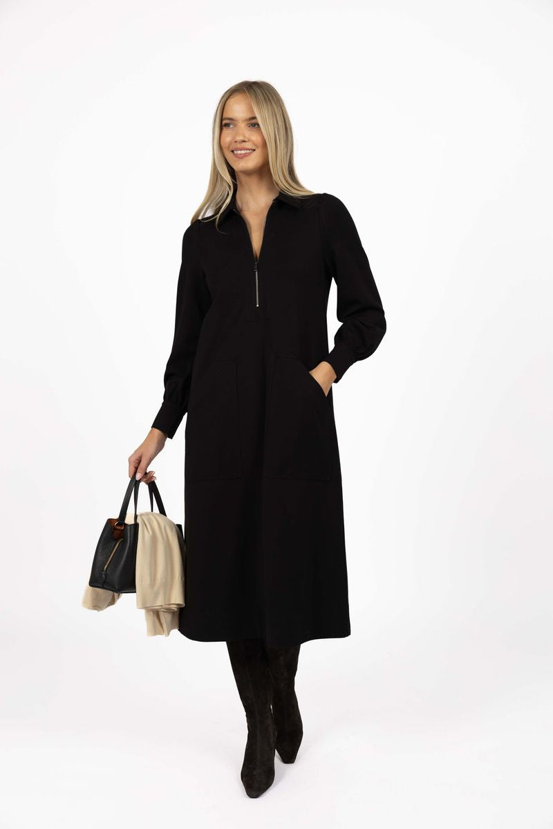 Model in studio wearing Dune Midi Dress in Black with black boots holding a black bag, full-length front view 
