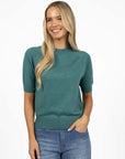Model in studio wearing Aurora Top in Turquoise with Ryder Jean, close-up front view with one hand in jean pocket  