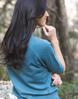 Model in lifestyle setting wearing Aurora Top in Turquoise, close-up back view with nature background 