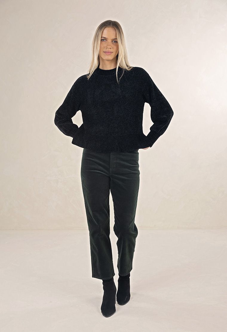 Model in studio wearing Chenille Jumper in Black with Va Va Velour Pant in Pine and black boots, full-length front view 