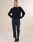 Model in studio wearing Chenille Jumper in Black with Va Va Velour Pant in Pine and black boots, full-length front view 