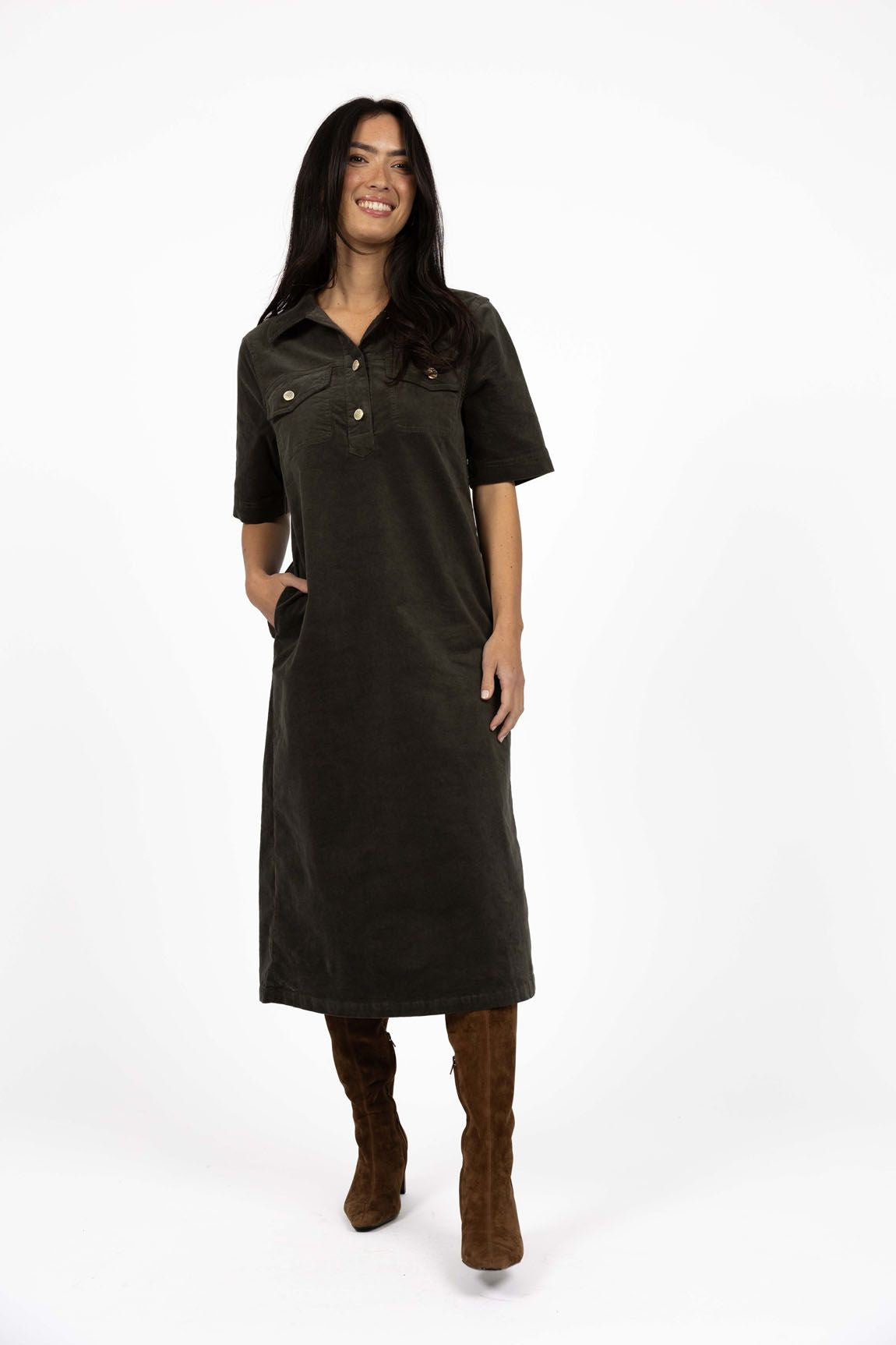 Model in studio wearing Amici Cord Dress in Khaki with brown boots, full-length front view with one hand in pocket  