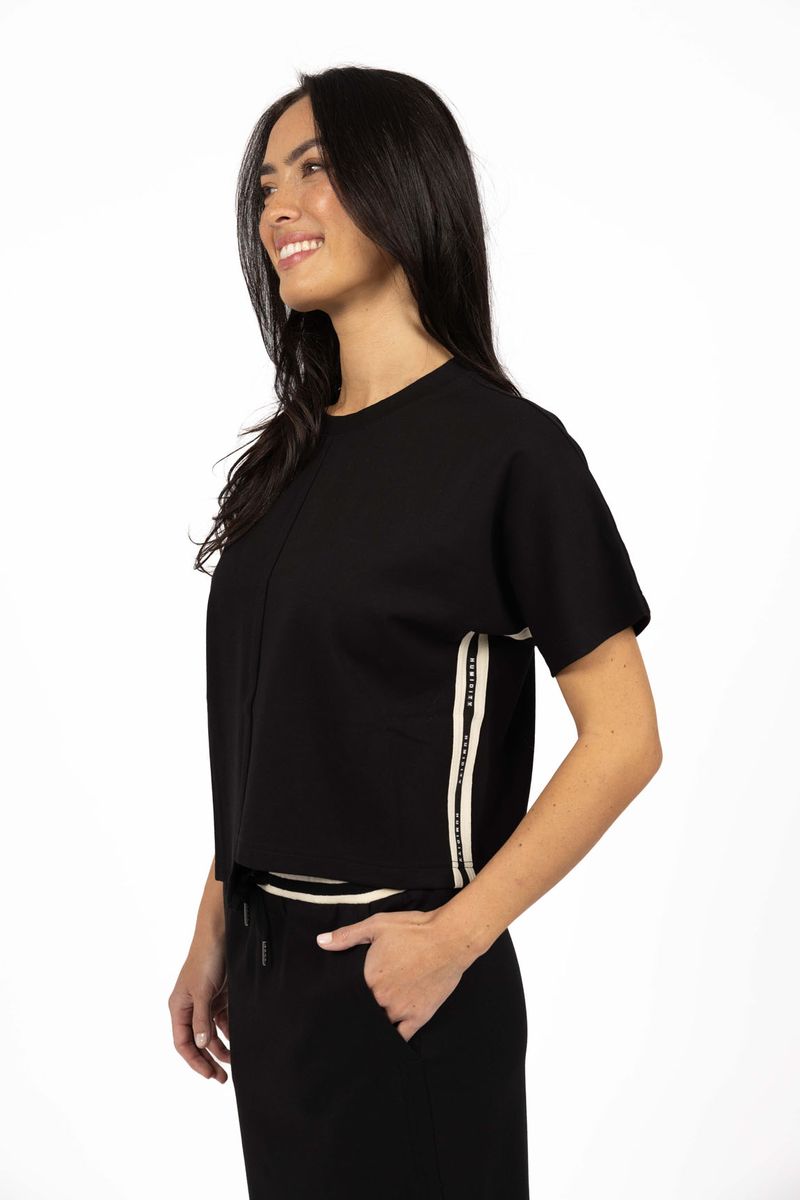 Model in studio wearing Mosh Top in Black with matching Roca Skirt, close-up side view showing branded tape detail on side seam 