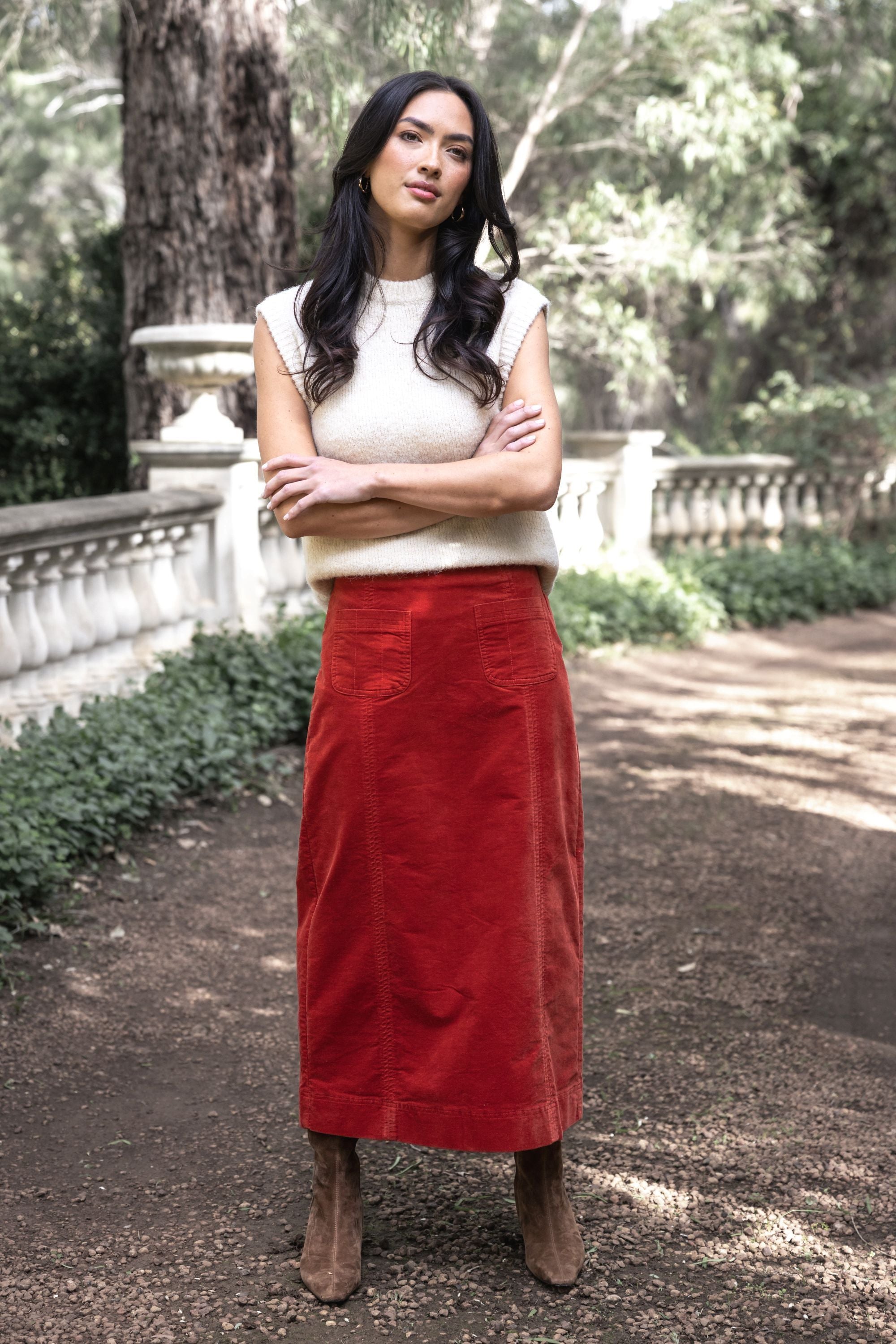 Model in lifestyle setting wearing Va Va Velour skirt in Rust with Monet Vest in Cream and brown boots, full-length front view with forest background 