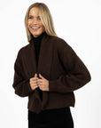 Model in studio wearing Liana Cardi in Chocolate over black skivvy, close-up front view holding lapels