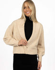 Model in studio wearing Liana Cardi in Oat over black skivvy, close-up front view showing brass pin closure  