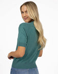 Model in studio wearing Aurora Top in Turquoise with Ryder Jean, close-up back view looking over shoulder  