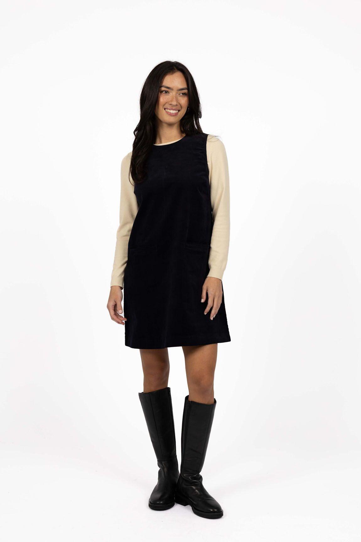 Model in studio wearing Nova Cord Dress in Indigo over the Mae Jumper in Buttermilk with black boots, full-length front view 