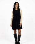 Model in studio wearing Nova Cord Dress in Indigo over the Mae Jumper in Buttermilk with black boots, full-length front view 