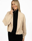 Model in studio wearing Liana Cardi in Oat over black skivvy, close-up front view holding collar  