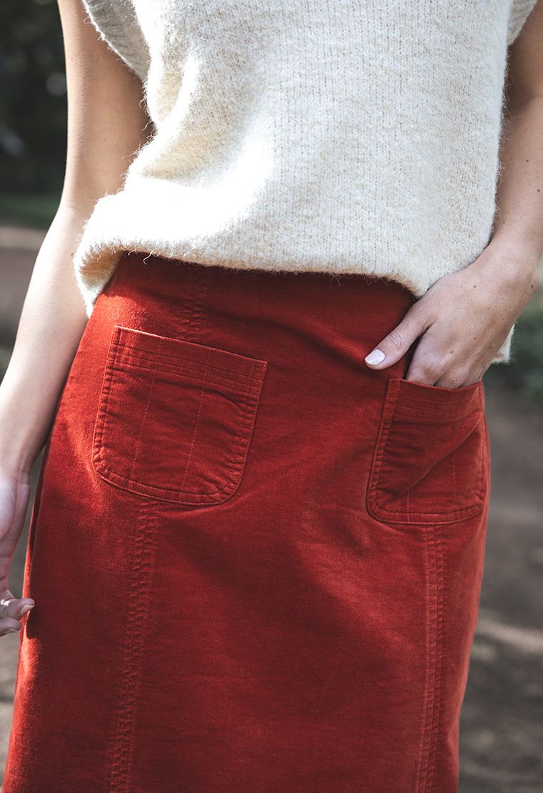 Model in lifestyle setting wearing Va Va Velour skirt in Rust with Monet Vest in Cream, close-up front view showing patch pockets  