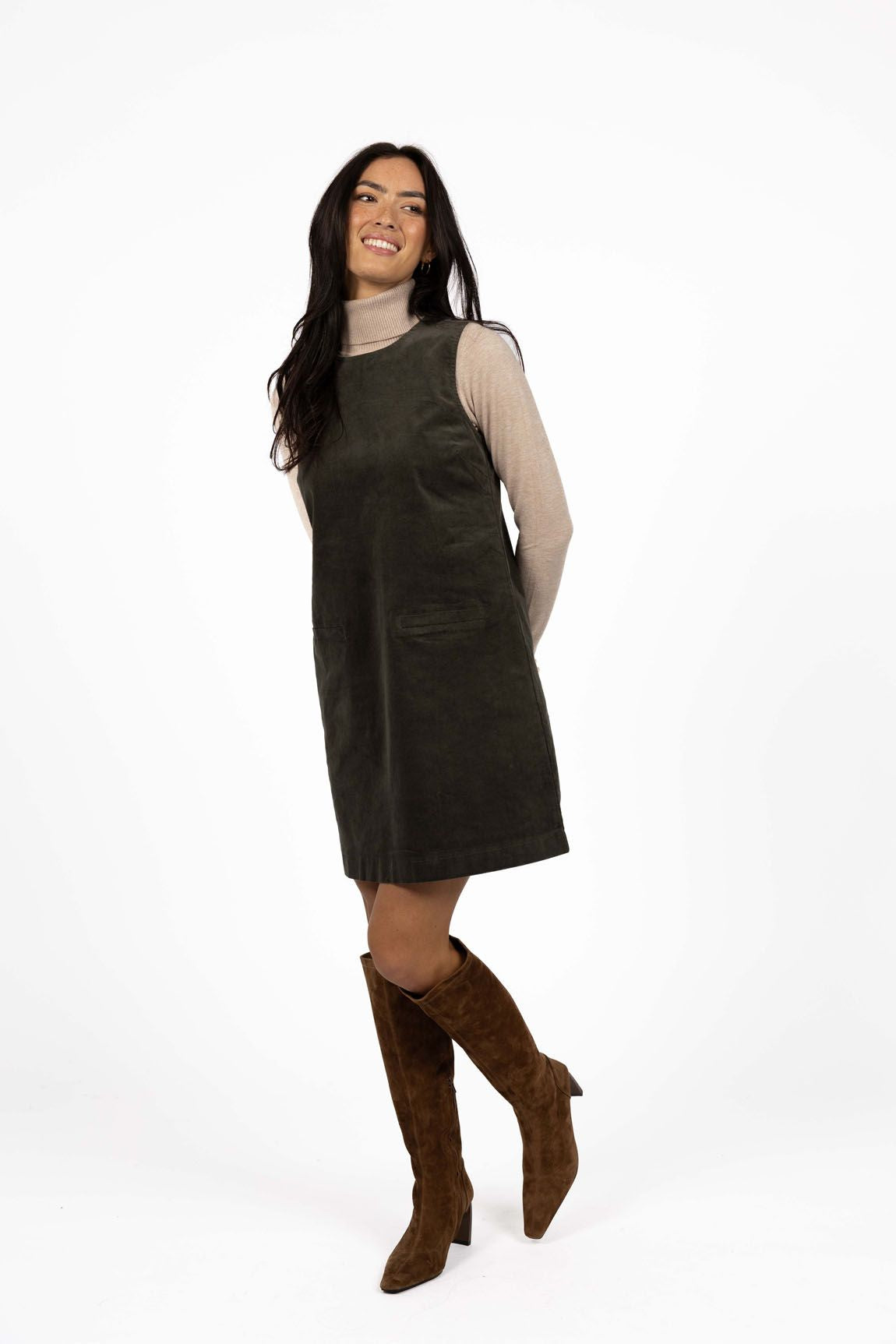 Model in studio wearing Nova Cord Dress in Khaki over the Alana Skivvy in Birch with brown boots, full-length front view 