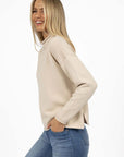 Model in studio wearing Divine Jumper in Stone with Ryder Jean, close-up side with one hand in pocket 